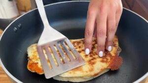 Person cooking a golden-brown quesadilla in a pan using a spatula.