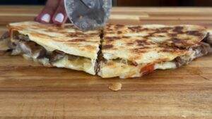 Sizzling quesadilla with cheese, mushrooms, and veggies being sliced on a wooden board. Perfect for a savory snack!