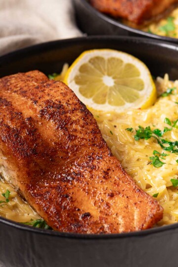 Lemon Salmon Orzo pasta garnished with lemon slice and parsley in a black bowl.