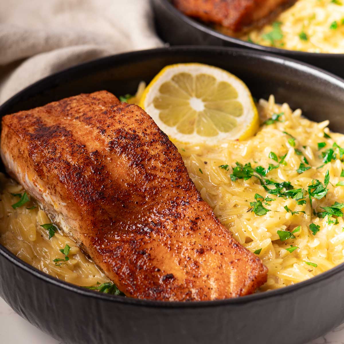 Lemon Salmon Orzo pasta garnished with lemon slice and parsley in a black bowl.