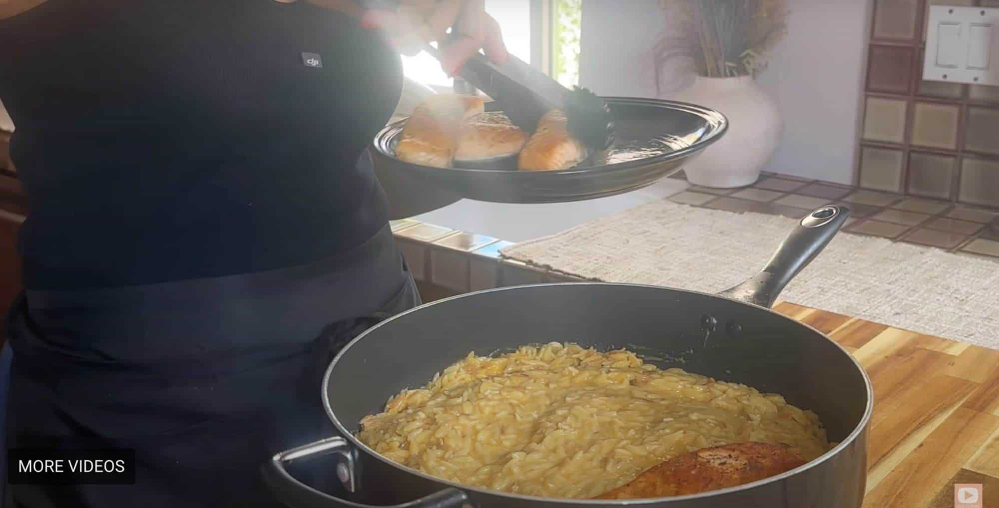 Chef plating grilled salmon over creamy orzo in a kitchen setting.