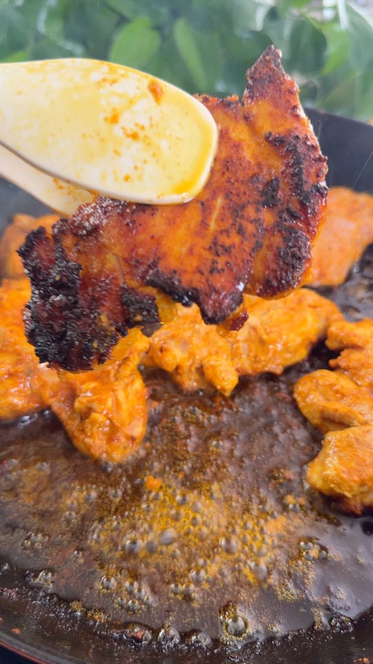 Cooking marinated chicken pieces in a pan with oil bubbling, one piece held by tongs.