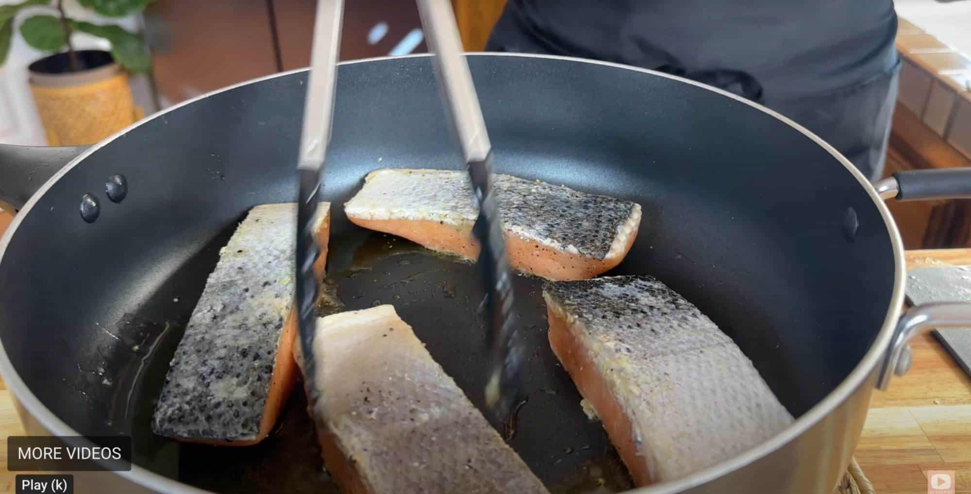 Cooking salmon fillets in a non-stick pan, skin-side down, with tongs.