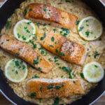 Pan-seared salmon with creamy lemon orzo, garnished with parsley and lemon slices in a skillet.