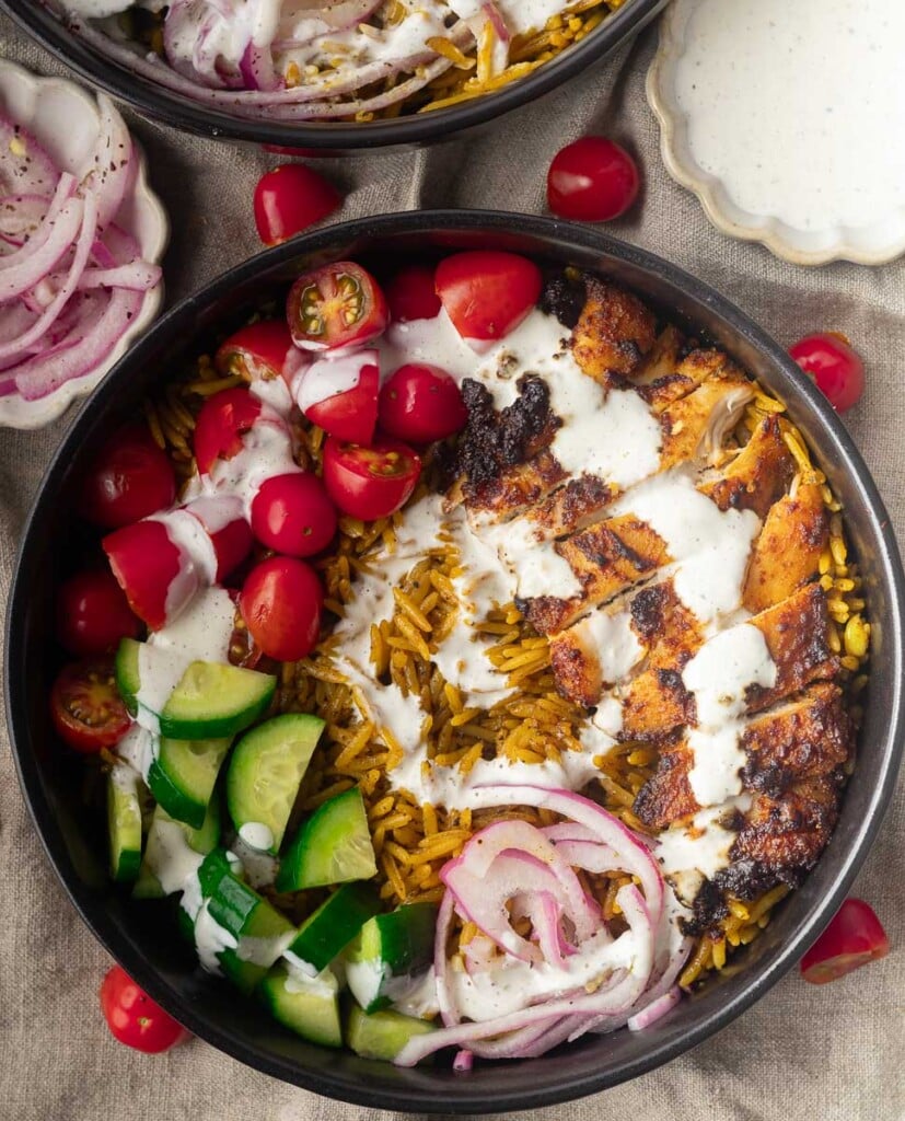 One pot shawarma and rice with grilled chicken bowl with rice, cherry tomatoes, cucumbers, red onions, and white sauce drizzle.