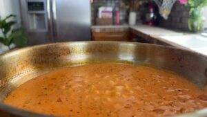 Simmering pot of rich tomato curry in a kitchen, highlighting delicious homemade cooking.