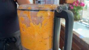 Food processor blending orange mixture in kitchen setting.