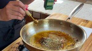 Adding organic oregano to sizzling oil in a skillet for delicious seasoning. Cooking spices and herbs in a pan.