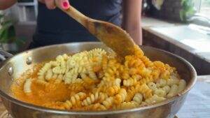 Person stirring fusilli pasta with creamy tomato sauce in a skillet.