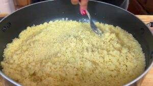 Stirring fluffy couscous in a pan with a fork for a perfect side dish.