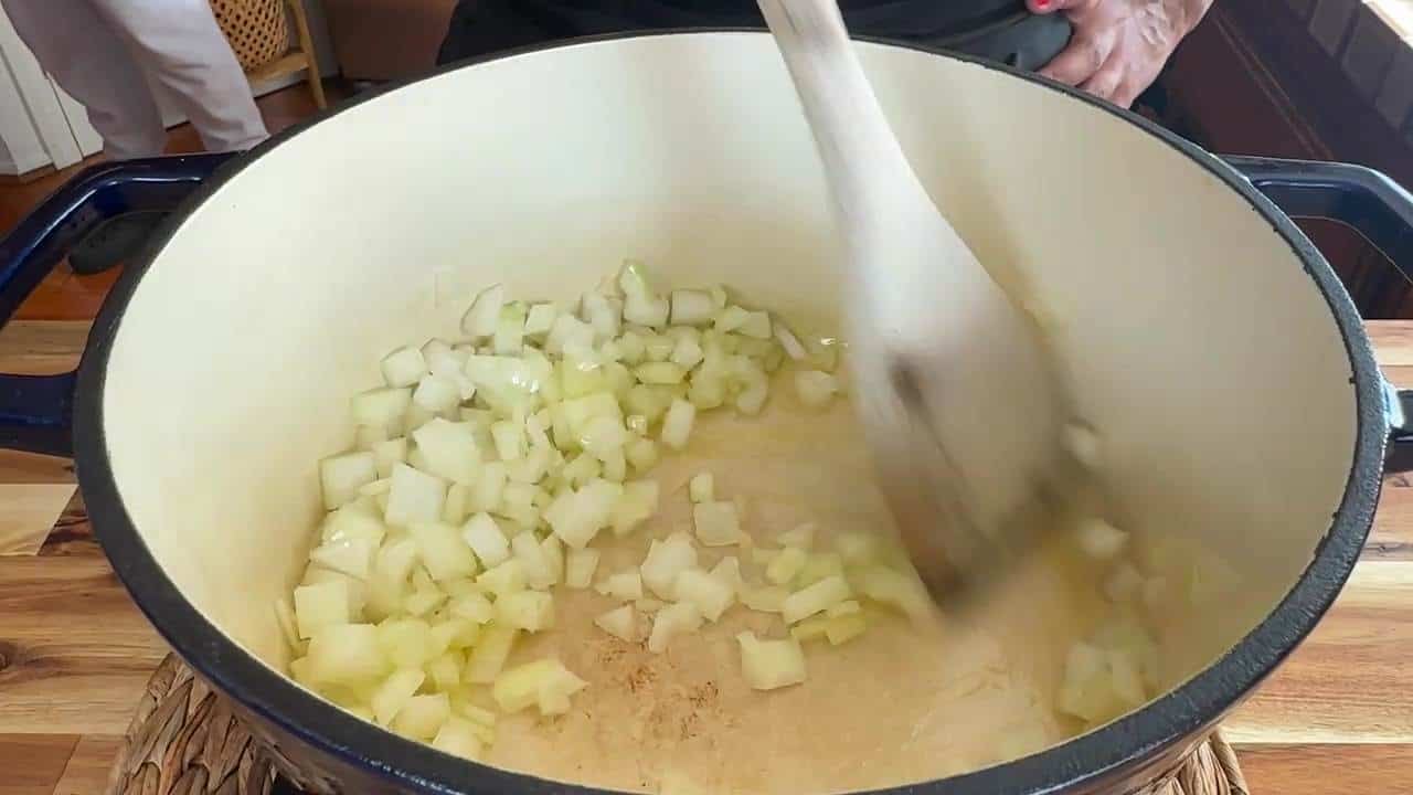 Cooking diced onions in a large pot with a wooden spoon, perfect for soups or stews.