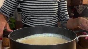 Person stirring creamy sauce in a pot in a cozy kitchen setting.