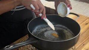 Person adding sauce to a non-stick pan on a wooden surface, preparing a meal.