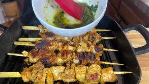 Grilling juicy chicken skewers with herb marinade in a black skillet.