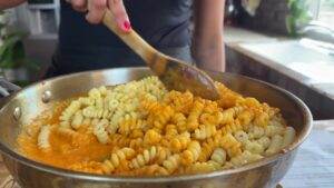 Person stirring creamy rotini pasta with sauce in a pan.