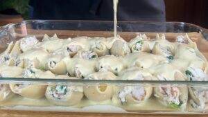 Cheesy stuffed pasta shells in a glass dish, covered with creamy sauce, ready for baking. Perfect Italian comfort food.