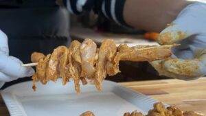 Grilled chicken skewers with spices being prepared on a wooden board by gloved hands.