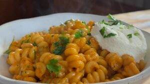 Creamy rotini pasta with rich tomato sauce, topped with fresh parsley and ricotta in a white bowl. Perfect comfort food.