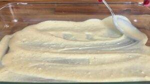 Spreading creamy batter in a glass baking dish with a spoon for a delicious recipe preparation.