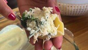 Person holding stuffed pasta shell with cheese and spinach filling, close-up view.