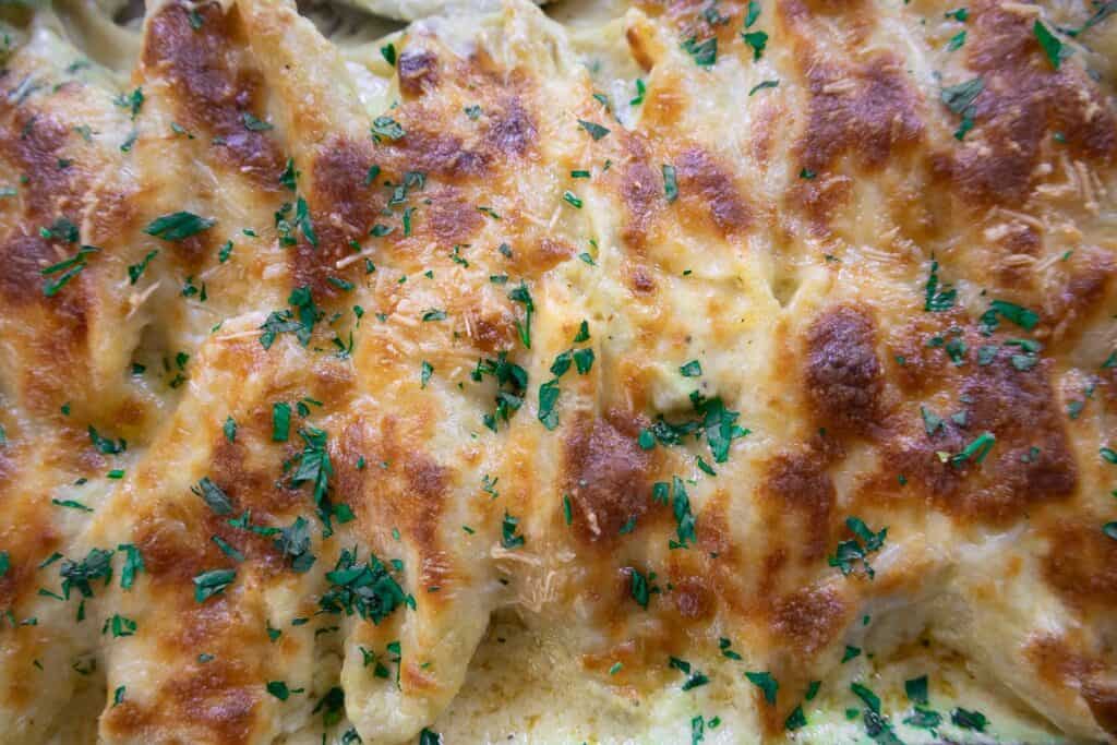 Close-up of golden baked cheesy pasta topped with fresh parsley, capturing its delicious texture and savory appeal.