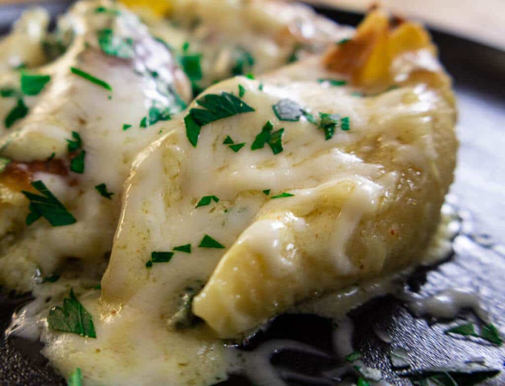 Cheesy stuffed pasta shells topped with melted cheese and fresh herbs on a black plate.