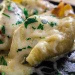 Cheesy stuffed pasta shells topped with melted cheese and fresh herbs on a black plate.