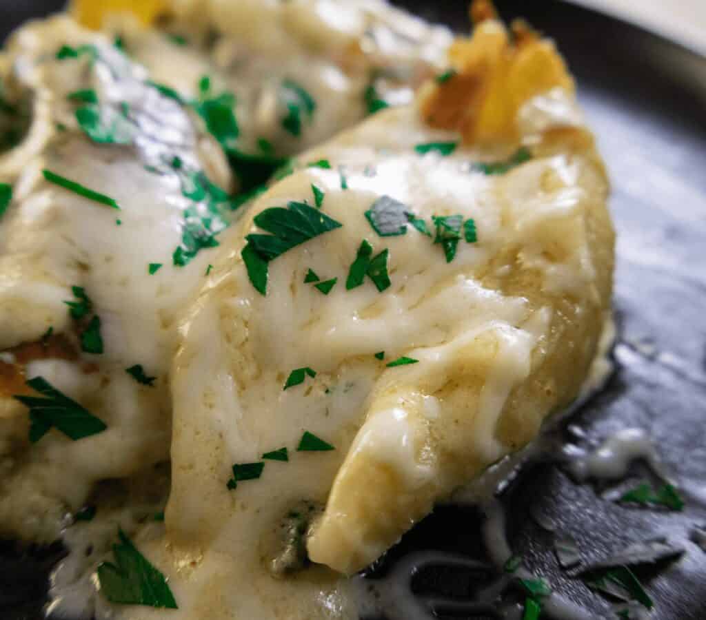 Cheesy stuffed pasta shells topped with fresh parsley on a black plate.