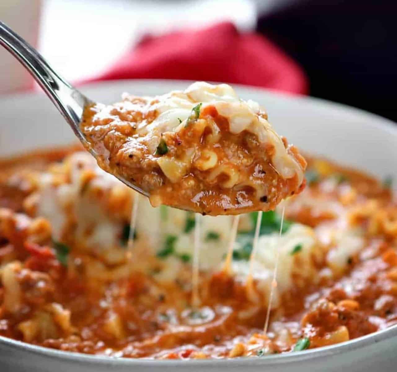 Cheesy lasagna soup in a spoon with melted cheese, highlighting its creamy texture and rich, savory flavors.