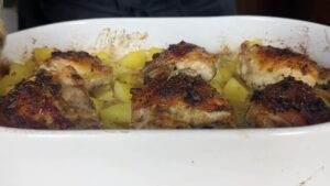 Roasted chicken thighs with herbs and potatoes in a white casserole dish, perfect for a flavorful family dinner.