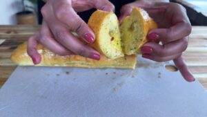 Person holding fresh garlic bread, revealing its buttery and herb-filled interior on a cutting board.