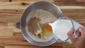 Mixing milk into dough ingredients in a metal bowl for baking on a wooden surface.