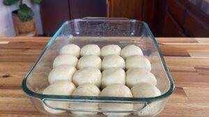 Glass baking dish with uncooked dough balls on a wooden kitchen counter. Perfect for homemade rolls.