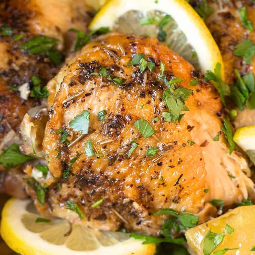 Close-up of seasoned baked chicken with fresh herbs and lemon slices.