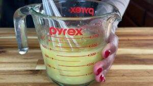 Hand mixing lemon juice in a Pyrex measuring cup on a wooden table for cooking or baking.