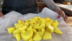 Chopped yellow potatoes on parchment paper, ready for roasting in a kitchen setting.