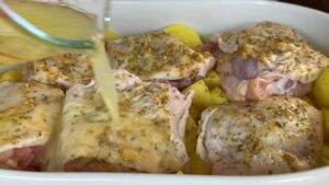 Pouring broth over seasoned chicken and potatoes in a baking dish for a savory oven-baked meal.