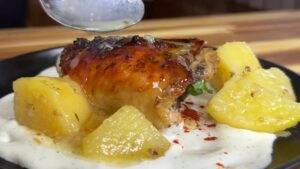 Roasted chicken with creamy sauce and potatoes on a plate, drizzled with sauce for a delicious meal.