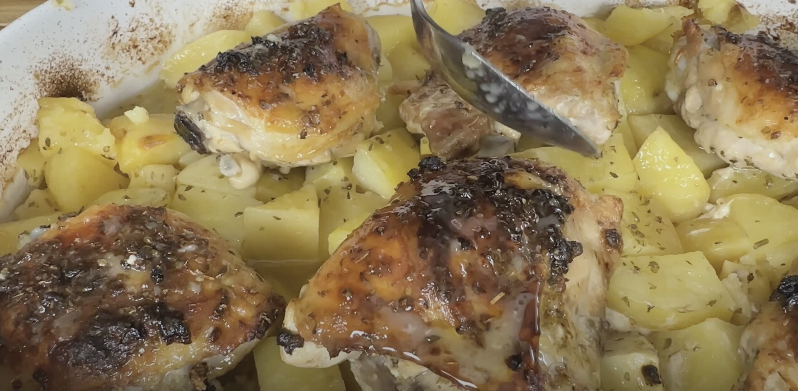 Baked chicken thighs with crispy skin served over roasted potatoes drizzled with herb seasoning.