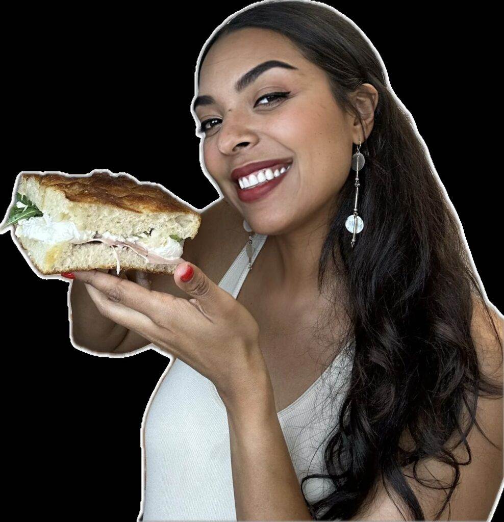 Person smiling while holding a large sandwich with fresh ingredients, highlighting delicious homemade food.
