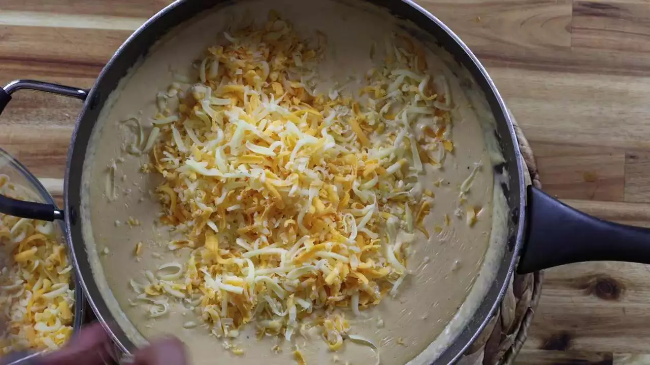 Pan of creamy cheese sauce topped with shredded cheddar and mozzarella on a wooden table.