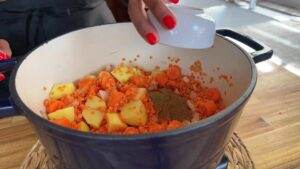 Cooking a hearty lentil stew with carrots, potatoes, and spices in a blue pot.