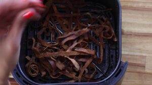 Air fryer with crispy potato peels being tossed, ready for a healthy snack.