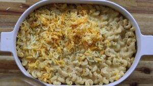 Creamy macaroni and cheese topped with shredded cheddar in a white baking dish on a wooden table.