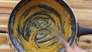 Whisking a smooth pumpkin mixture in a pan on a wooden countertop, perfect for a cozy autumn recipe.