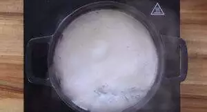 Pot of milk boiling on a stovetop, creating steam, viewed from above.