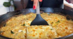 Delicious cheesy lasagna slice being served with a spatula from a cast iron skillet.