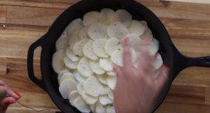 Sliced potatoes being arranged in a cast iron skillet for a delicious gratin recipe.