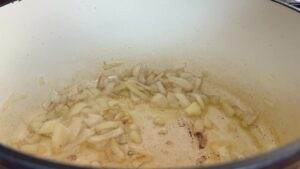 Chopped onions sautéing in a large pot, releasing aroma for a savory dish preparation.