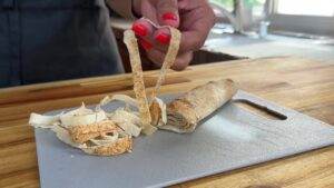 Person preparing fresh noodle strips on a cutting board with rolled dough in the kitchen.